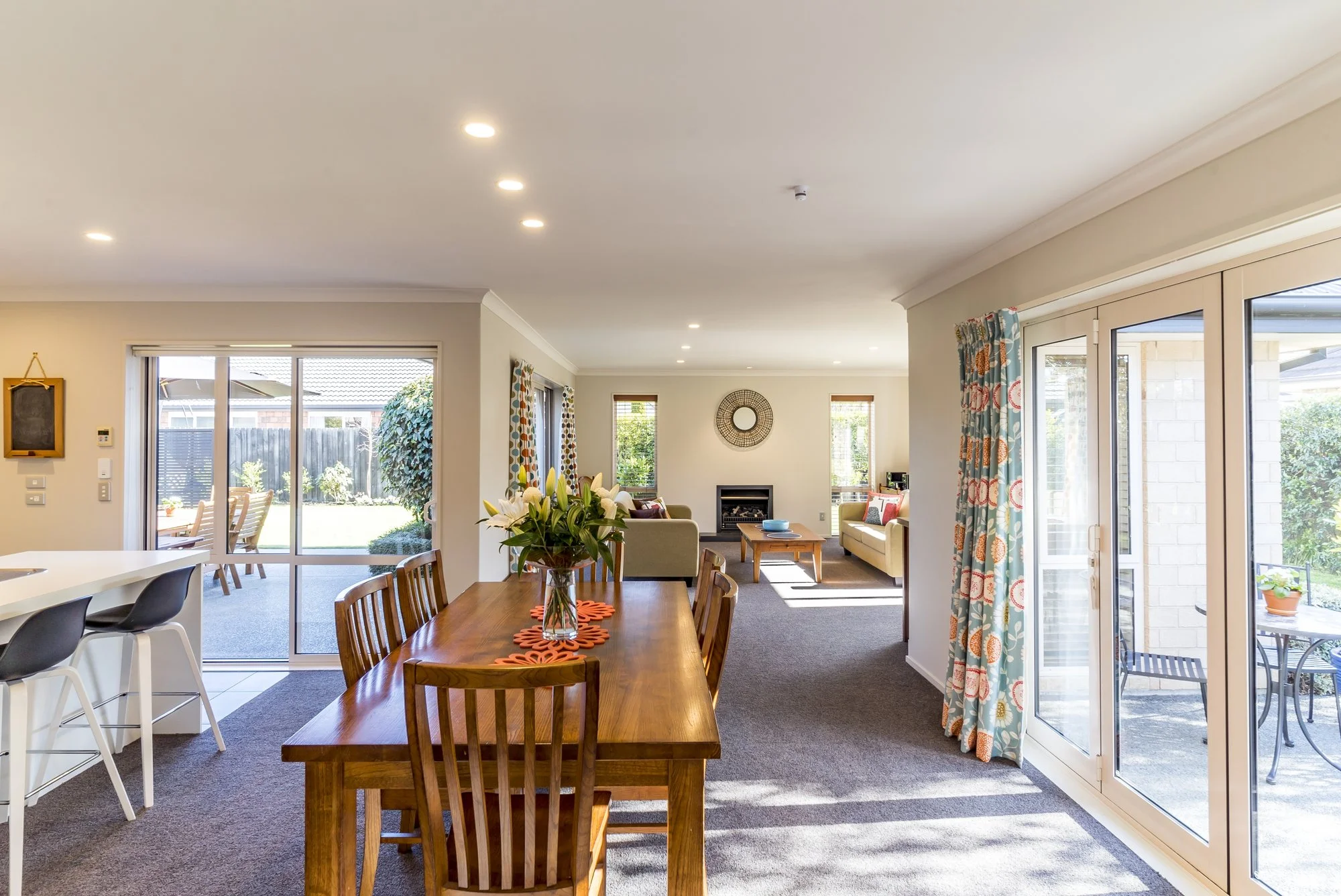 Open-plan dining room with a wooden table, bar stools and glass doors to a garden