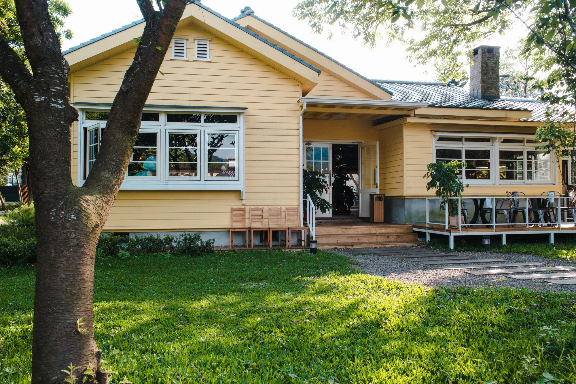 Yellow wooden house with large windows, a porch and a green lawn